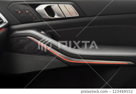Door handle with power window control buttons. Black perforated leather interior with stitching. Modern car black leather interior details. 123489552