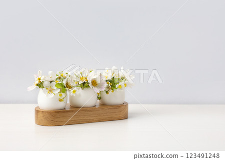 Three white eggs in a stand with spring pear and strawberry flowers on a gray background. Happy Easter 123491248