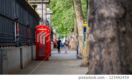 A red telephone booth on a peaceful London sidewalk, framed by trees, brings together the charm of the city past and its natural beauty. A red telephone booth on a peaceful London sidewalk, framed by trees, brings together the charm of the city past and its natural beauty. 123492459