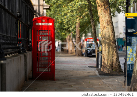 A red telephone booth on a peaceful London sidewalk, framed by trees, brings together the charm of the city past and its natural beauty. 123492461
