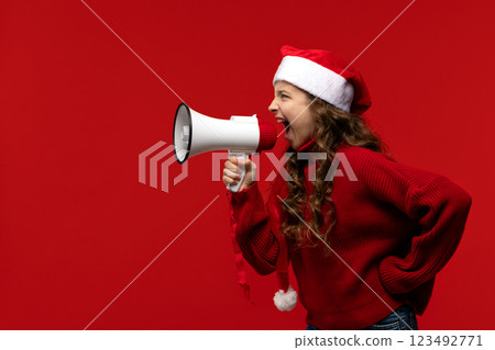 Energetic girl in Santa hat and sweater shouts into megaphone Energetic girl in Santa hat and sweater shouts into megaphone 123492771