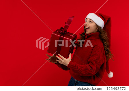 Excited girl in Santa hat catches large red Christmas gift. 123492772