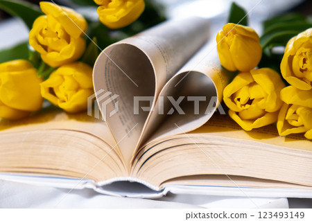 Book pages in shape of heart symbol love with bouquet of pink tulips on messy bed. Romantic morning scene. Greeting card Holiday flowers springtime Book pages in shape of heart symbol love with bouquet of pink tulips on messy bed. Romantic morning scene. Greeting card Holiday flowers springtime 123493149