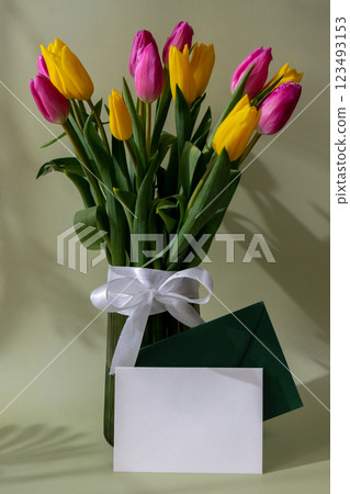 Empty white envelope mock up template Multicolored fresh tulips in vase in green background with trendy deep shadows. Spring flowers in yellow and violet colors. Postcard wallpaper design Empty white envelope mock up template Multicolored fresh tulips in vase in green background with trendy deep shadows. Spring flowers in yellow and violet colors. Postcard wallpaper design 123493153