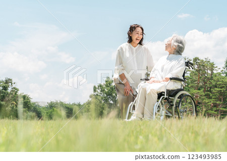 A senior woman in a wheelchair in a park and a woman assisting her (nursing care, parent and child, elderly care home) 123493985