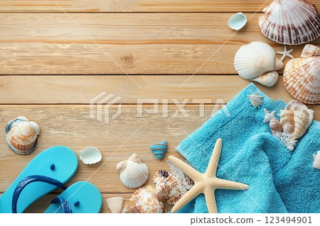 Different seashells with towels and flip flops on brown wooden table 123494901
