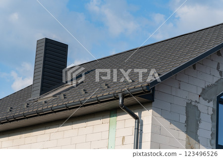 The modern house showcases a newly installed tiled roof, complemented by a sleek chimney structure under bright, sunny skies, enhancing its architectural elegance The modern house showcases a newly installed tiled roof, complemented by a sleek chimney structure under bright, sunny skies, enhancing its architectural elegance 123496526