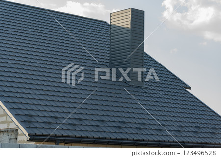 The modern house features a stylish tiled roof with a prominent chimney. The clean lines and contemporary design highlight the architecture against a clear blue sky 123496528