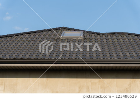 The stylish roof of a contemporary house showcases a sleek tiled design with a skylight, harmonizing with the blue sky above, highlighting modern architectural aesthetics 123496529