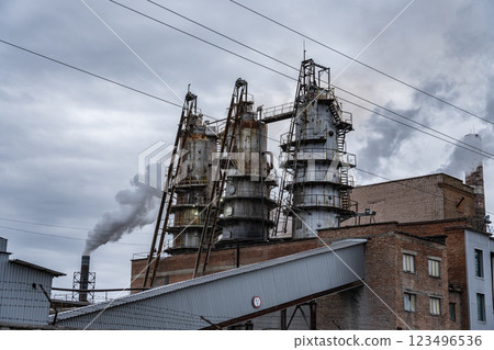 Dark smoke rises from tall smokestacks of an industrial manufacturing plant under a cloudy sky, showcasing the facility's emissions and activity 123496536