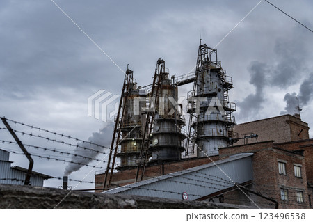 Thick smoke is released from the tall smokestacks of an industrial facility, indicating ongoing production. The sky is overcast, adding to the somber atmosphere 123496538