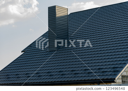 A sleek and modern roof features black metal tiles that reflect sunlight, highlighting the contemporary design of the house and its chimney structure 123496548