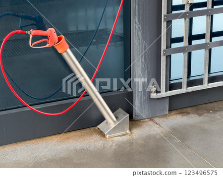 A high-pressure car washer gun stands ready at a car wash, featuring sleek metal design and vibrant red hose, ensuring thorough cleaning of vehicles in progress 123496575