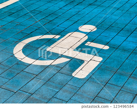 A designated parking spot for disabled individuals is clearly marked on the ground with a white symbol against a blue pavement surface, ensuring accessibility for all A designated parking spot for disabled individuals is clearly marked on the ground with a white symbol against a blue pavement surface, ensuring accessibility for all 123496584