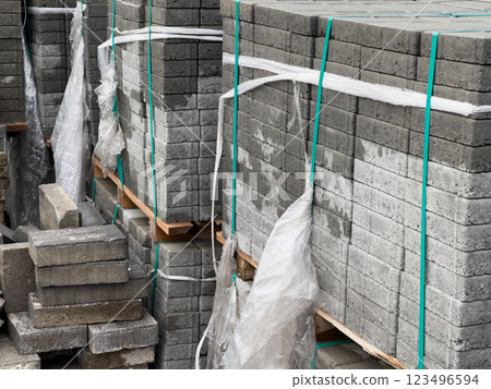 Stacks of gray cobblestone blocks secured with plastic wrap and ropes, prepared for use in a sidewalk construction project in an urban environment Stacks of gray cobblestone blocks secured with plastic wrap and ropes, prepared for use in a sidewalk construction project in an urban environment 123496594