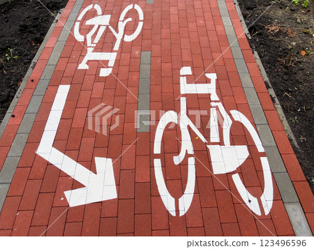 A clearly marked bike lane sign is painted on a red brick sidewalk, providing direction for cyclists in an urban environment with green surroundings A clearly marked bike lane sign is painted on a red brick sidewalk, providing direction for cyclists in an urban environment with green surroundings 123496596