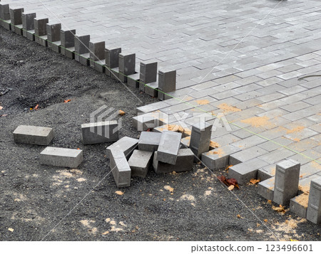 A crew is laying down paving stones to repair a section of pavement. The stones are gray and rectangular, and they are being laid in a pattern. The area around the stones is covered in gravel A crew is laying down paving stones to repair a section of pavement. The stones are gray and rectangular, and they are being laid in a pattern. The area around the stones is covered in gravel 123496601