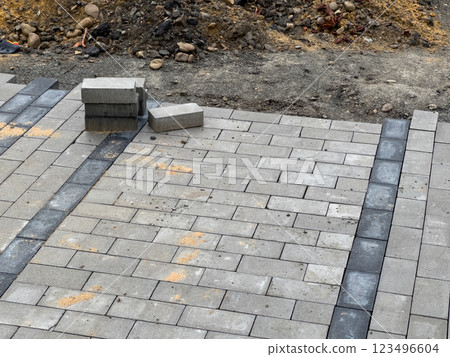 A section of pavement being repaired with gray paving stones. There are a few stones that have been laid in a row, but most of the area is still bare 123496604