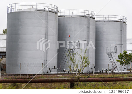 Three large gray storage tanks are positioned closely together at an industrial site. Metal catwalks and ladders provide access for maintenance and monitoring Three large gray storage tanks are positioned closely together at an industrial site. Metal catwalks and ladders provide access for maintenance and monitoring 123496617