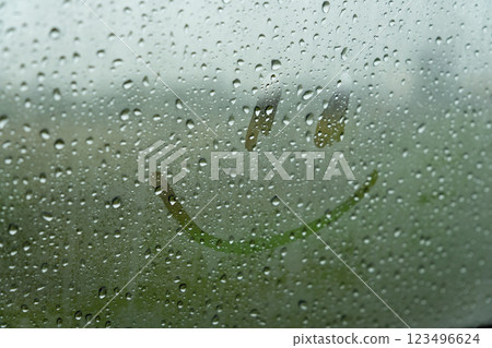 A simple smiley face is drawn on a foggy car window, surrounded by droplets of rain. The artwork brightens the dreary atmosphere on a rainy day 123496624