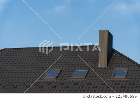 The rooftop showcases interlocking gray tiles, featuring three skylights beneath a clear blue sky. A wooden chimney rises prominently from the roofline, adding to the structure's charm The rooftop showcases interlocking gray tiles, featuring three skylights beneath a clear blue sky. A wooden chimney rises prominently from the roofline, adding to the structure's charm 123496659