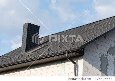 This house showcases a newly installed black metal tile roof, enhancing its modern design. A prominent chimney adds character against the clear sky 123496662
