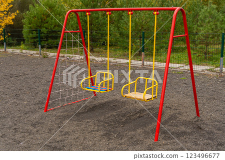 The playground features a bright red swing set with two seats, surrounded by a gravel area, perfect for children to enjoy swinging and outdoor playtime The playground features a bright red swing set with two seats, surrounded by a gravel area, perfect for children to enjoy swinging and outdoor playtime 123496677
