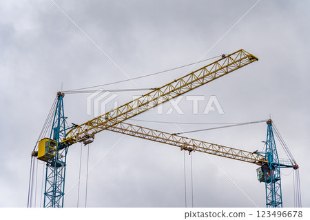 Two construction cranes are positioned at a construction site, actively working to lift heavy materials against a backdrop of overcast skies, indicating ongoing development efforts 123496678
