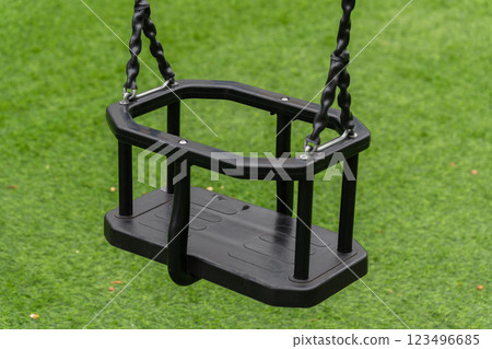 A secure swing for children, set in a lively playground with soft grass, perfect for outdoor fun and enjoyment during sunny afternoons 123496685
