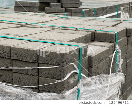Various stacks of concrete pavement blocks are secured with plastic wrap, awaiting use at a construction site. These materials are crucial for urban development projects 123496711