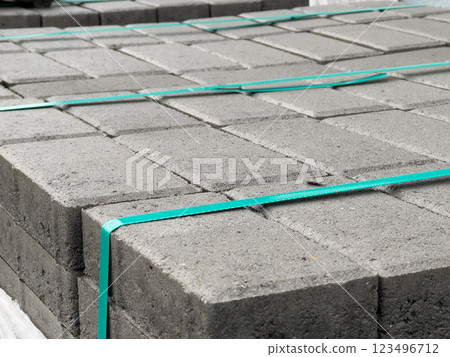 Concrete pavement blocks are arranged in neat stacks, secured with plastic straps, awaiting use in a construction project under clear skies Concrete pavement blocks are arranged in neat stacks, secured with plastic straps, awaiting use in a construction project under clear skies 123496712
