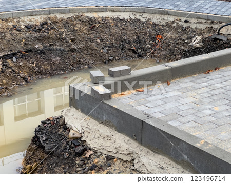 Workers are in the process of laying new pavement near a construction site where drainage problems have created a muddy area and exposed soil around the edges 123496714