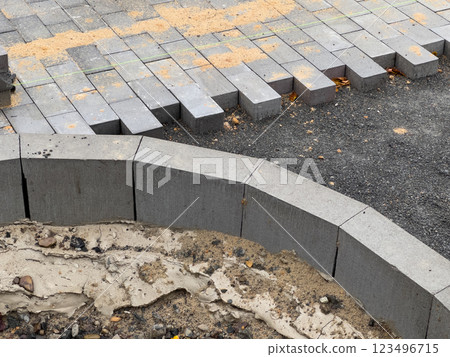 Workers are busy laying down paving stones in a construction area, where the bricks are neatly arranged, and sand is scattered nearby for leveling purposes 123496715