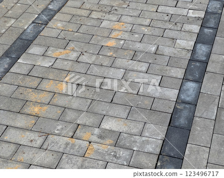 A gray brick pavement with black stripes. There is some dirt and debris on the bricks 123496717
