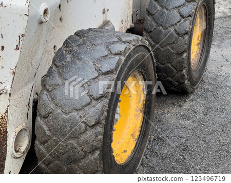 The heavy-duty tires of a bobcat are covered in mud, highlighting their use in a construction environment. The ground is gravelly and worn from activity throughout the day 123496719