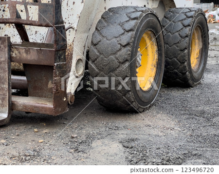 A bobcat tractor equipped with heavy tires is actively maneuvering through uneven ground at a construction site, showcasing its power and utility A bobcat tractor equipped with heavy tires is actively maneuvering through uneven ground at a construction site, showcasing its power and utility 123496720
