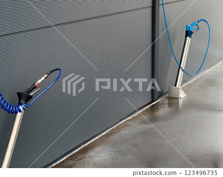 Two high-pressure car washer gun stands are positioned against a grey wall, equipped for cleaning vehicles efficiently in a well-lit automotive service space Two high-pressure car washer gun stands are positioned against a grey wall, equipped for cleaning vehicles efficiently in a well-lit automotive service space 123496735