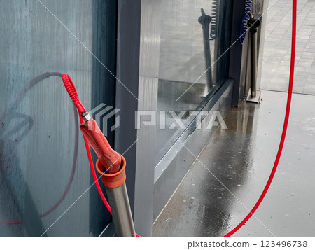 A high-pressure car washer gun stands ready for use at a self-service washing station, with droplets of water still glistening on the surface nearby 123496738