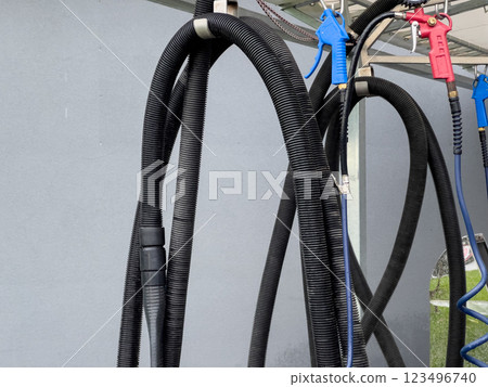 High pressure car washer guns and hoses are neatly organized at a car wash station, ready for use during busy service hours, ensuring efficient cleaning High pressure car washer guns and hoses are neatly organized at a car wash station, ready for use during busy service hours, ensuring efficient cleaning 123496740
