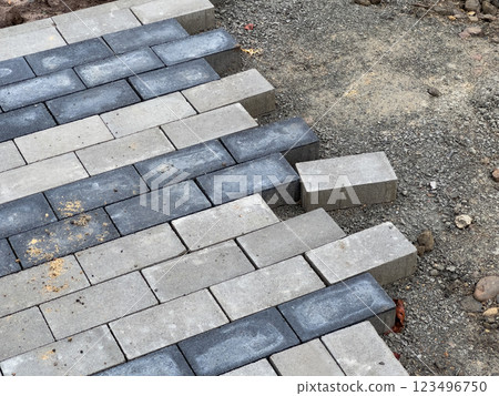 Workers carefully lay the paving stones in a pattern to construct a robust pavement at a construction site, ensuring precise alignment for durability 123496750
