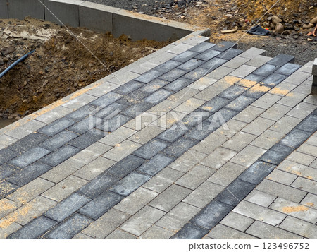 A team is actively laying paving stones to create a durable pathway in a residential area. The work is taking place during the day, showcasing the construction process A team is actively laying paving stones to create a durable pathway in a residential area. The work is taking place during the day, showcasing the construction process 123496752