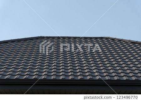 The meticulously installed metal roof tiles reflect the sunlight, creating a stunning juxtaposition against the expansive blue sky above, highlighting craftsmanship and durability 123496770
