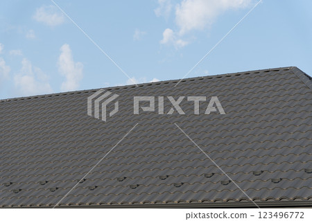 A sleek metallic roof glistens in the sunlight, reflecting the craftsmanship of modern tiling techniques against a backdrop of fluffy clouds and blue sky 123496772