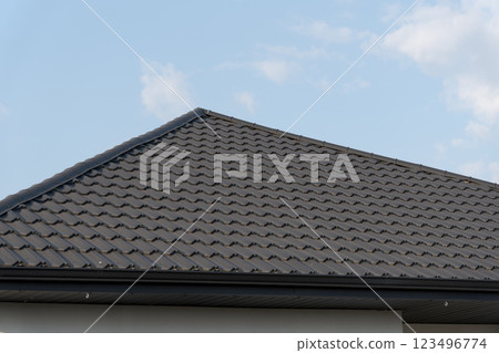 A striking rooftop features intricately arranged metallic tiles, glimmering under the warm sunlight, providing a stylish touch to the structure, set against a serene blue backdrop A striking rooftop features intricately arranged metallic tiles, glimmering under the warm sunlight, providing a stylish touch to the structure, set against a serene blue backdrop 123496774