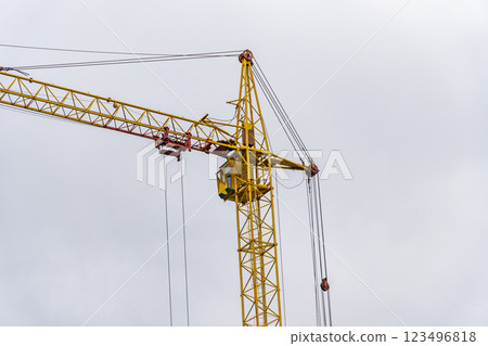 A large yellow crane lifts construction materials at a busy site under a cloudy sky, showcasing its essential role in heavy machinery operations and building projects 123496818