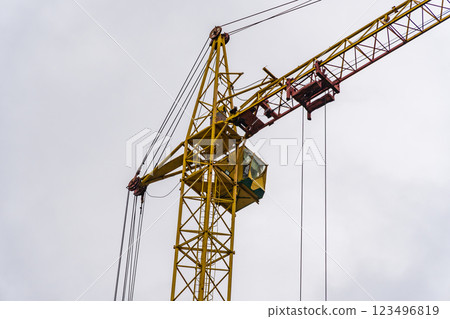 The crane is actively lifting heavy materials above a construction site, with workers visible in the cab, showcasing their work during overcast weather The crane is actively lifting heavy materials above a construction site, with workers visible in the cab, showcasing their work during overcast weather 123496819