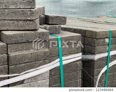 Gray brick pavers are neatly stacked and secured with straps, ready for use in paving a sidewalk on an urban street, indicating construction activity nearby 123496864