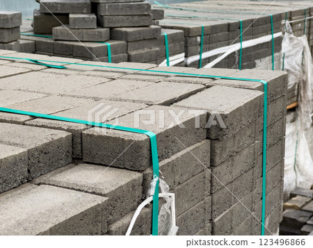 Gray brick pavers are neatly stacked and secured with plastic wraps, waiting for installation on a city sidewalk. The setup indicates ongoing urban development activities 123496866