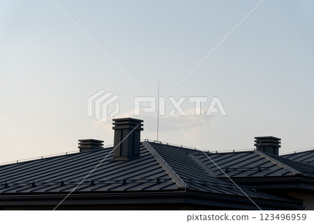 As the sun sets, a modern home's distinctive metal tile roof reflects soft hues of the sky. Tall chimneys add character while a delicate antenna reaches for the clouds, evoking tranquility As the sun sets, a modern home's distinctive metal tile roof reflects soft hues of the sky. Tall chimneys add character while a delicate antenna reaches for the clouds, evoking tranquility 123496959