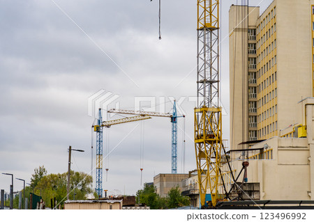 Amidst a moody sky, towering cranes stand vigil over a busy urban construction site, where workers bustle about, shaping the future of the city 123496992
